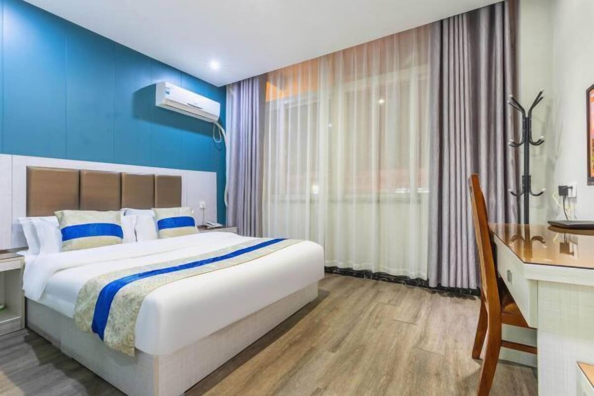 A hotel room with a bed, a desk, a chair, a coat rack, and a window with curtains.