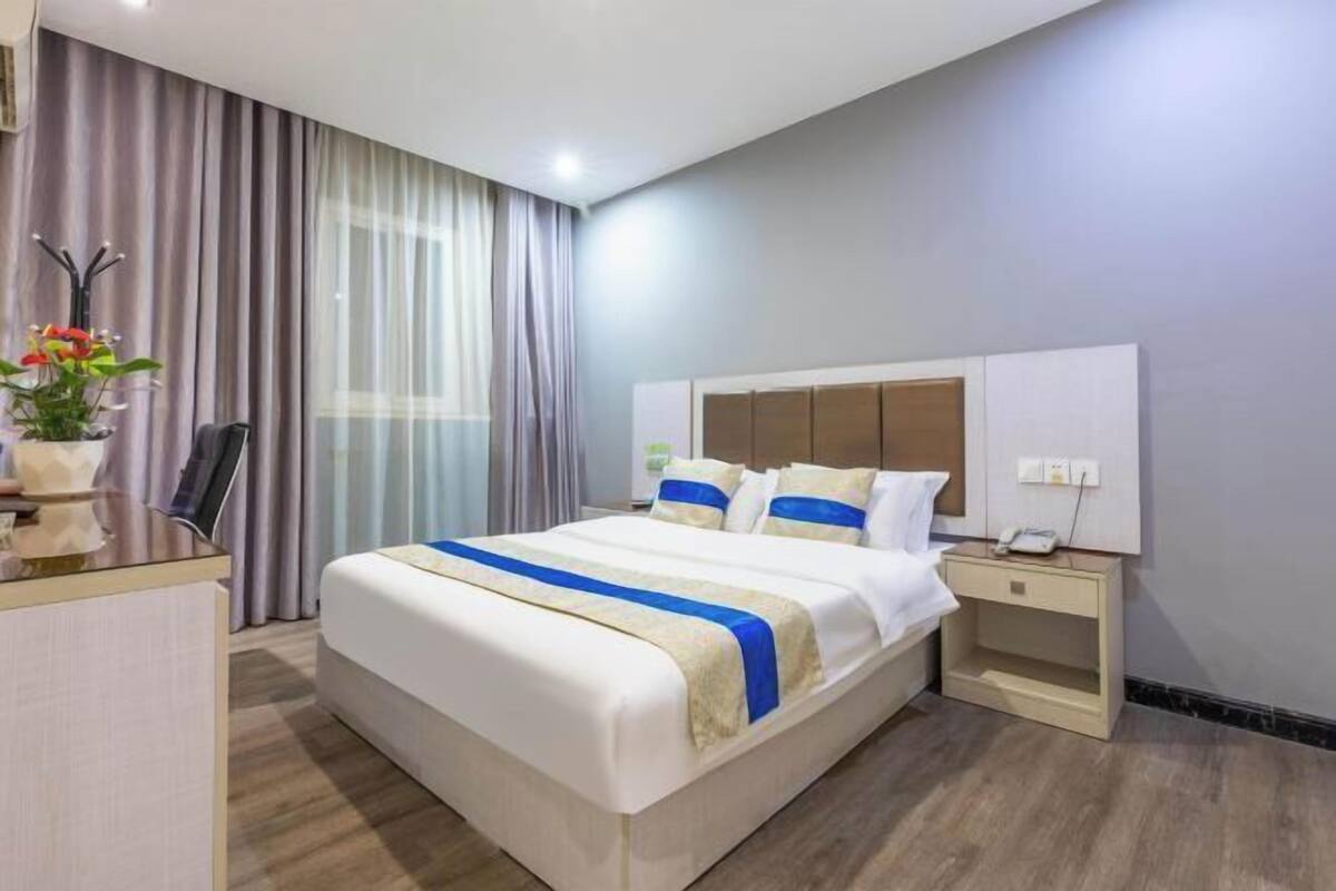 A hotel room with a large bed, bedside tables, a desk, and a window with curtains.