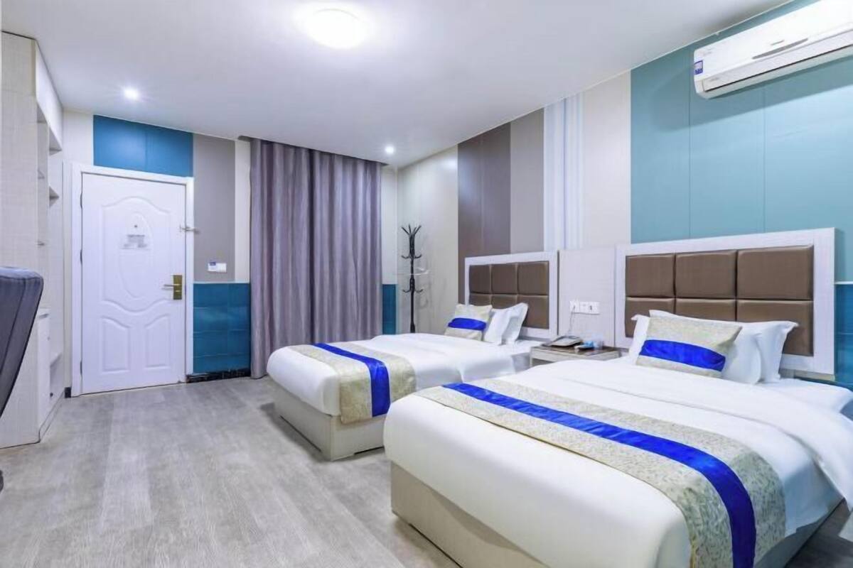 A hotel room with two beds, a wardrobe, a desk, and an air conditioning unit.