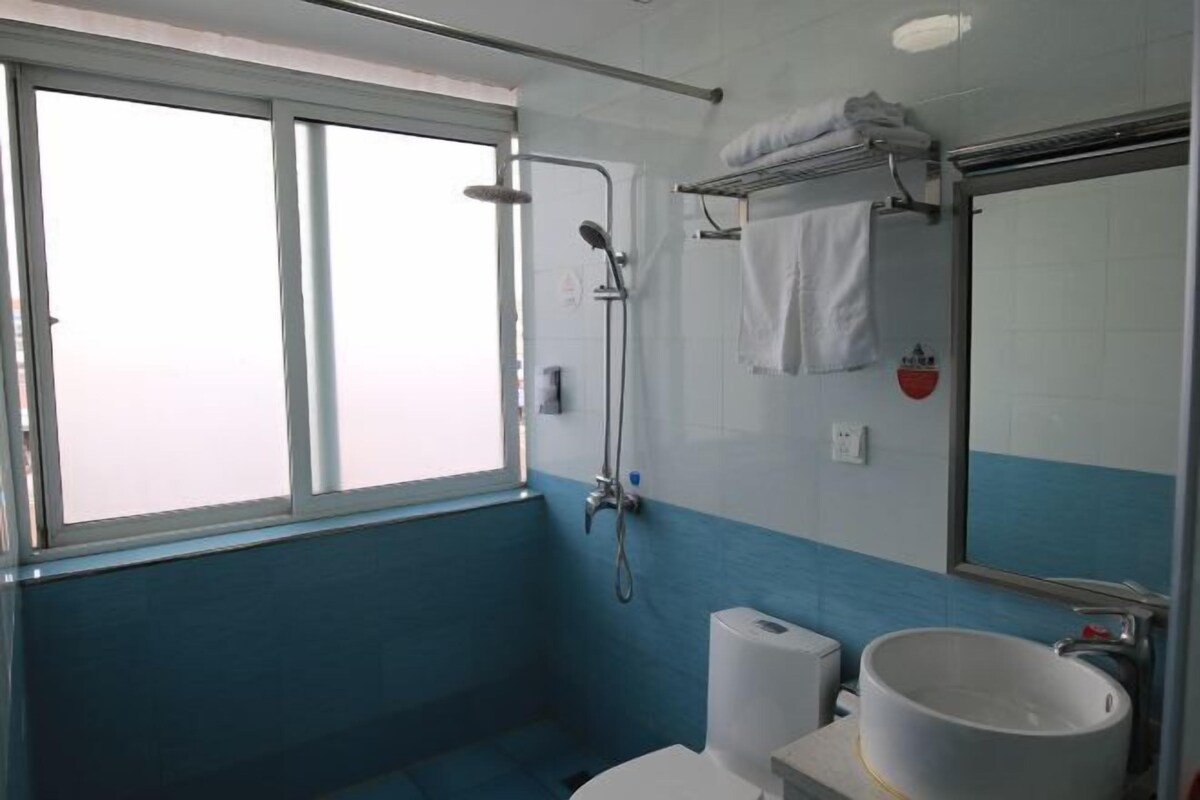 A bathroom with a window, a shower, a toilet, a sink, and a towel rack.
