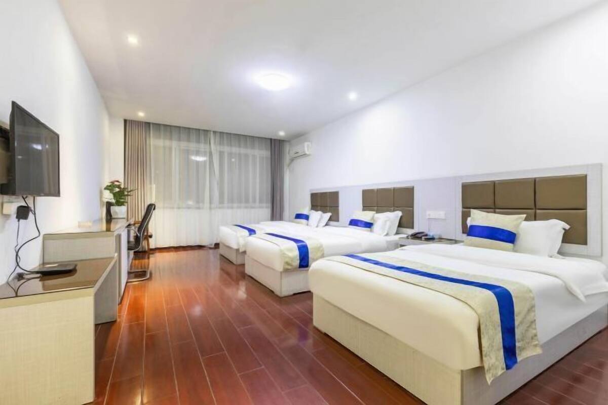 A hotel room with two beds, a desk, a TV, and a window with curtains.
