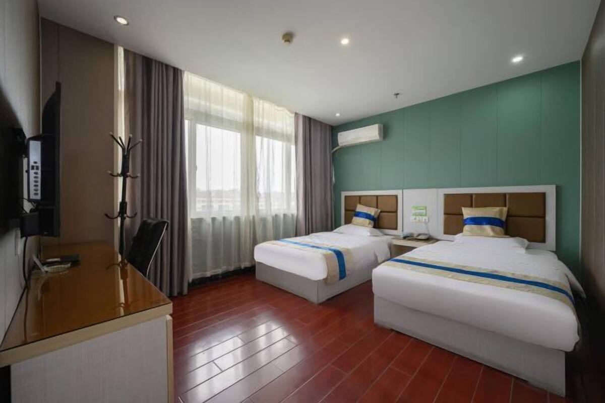 A hotel room with two beds, a desk, a TV, and a window with curtains.