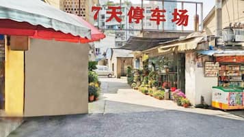 A street with a sign for a parking lot, a small shop, and a building with a red awning.