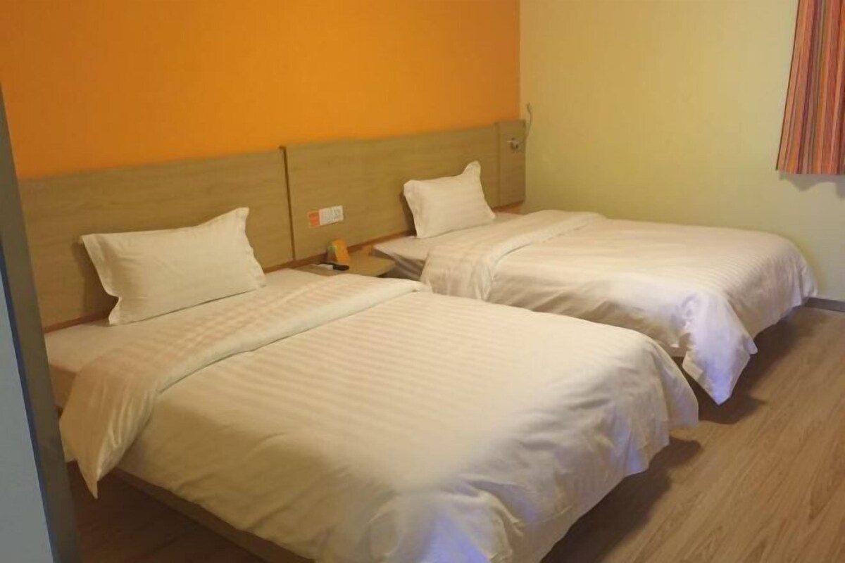 Une chambre d’hôtel avec deux lits simples, des têtes de lit en bois et un mur de couleur orange unie.