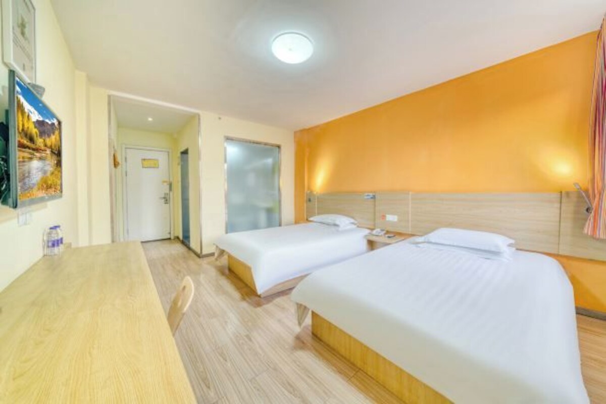 A hotel room with two beds, a wooden desk, and a painting on the wall.