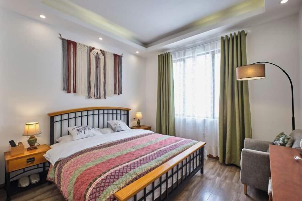 Une chambre à coucher avec un lit, des tables de chevet, une lampe, une chaise et une fenêtre avec des rideaux.