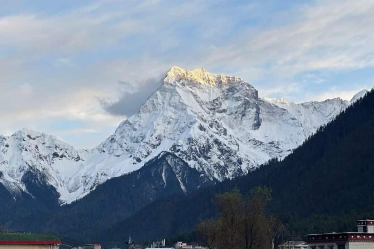 Une chaîne de montagnes enneigées, avec un sommet bien visible, un petit bâtiment doté d’un toit rouge et une zone boisée au premier plan.