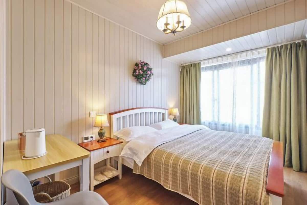 Une chambre d’hôtel avec un lit, des tables de chevet, une chaise, un bureau et une fenêtre avec des rideaux.