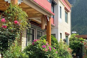 Ένα κτίριο με μπαλκόνι, περιτριγυρισμένο από πλούσια βλάστηση και ανθισμένα φυτά.