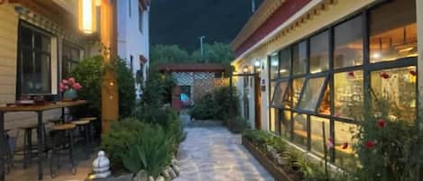Un patio con suelo de piedra, una zona de comedor y un edificio con grandes ventanales.