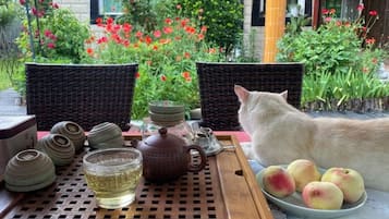 Una mesa con tetera, tazas y una fuente de fruta, al aire libre con sillas y un jardín al fondo.