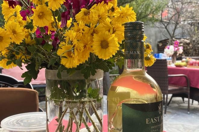 Una mesa con una botella de Jerez Dulce de las Indias Orientales y un jarrón con flores amarillas.