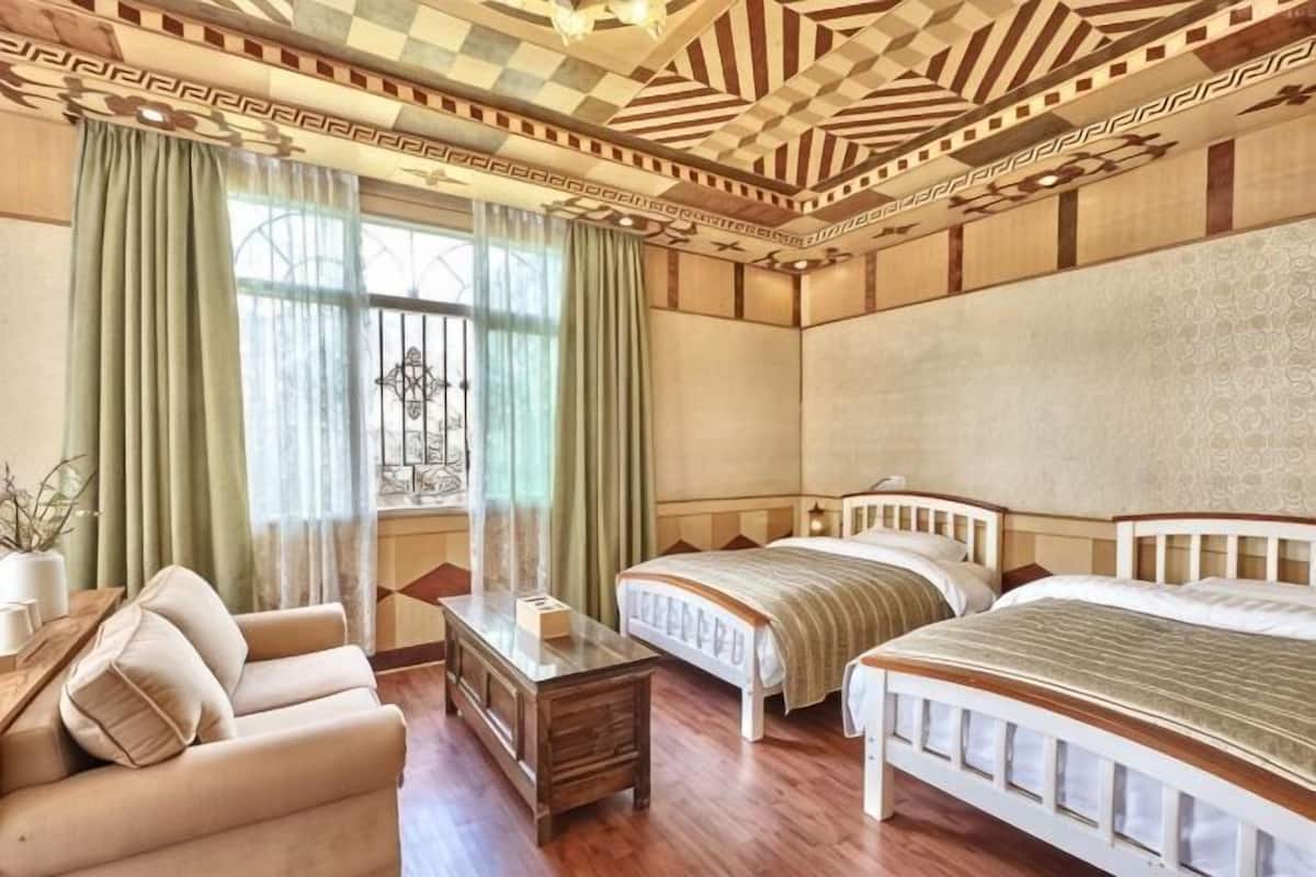 Une chambre avec deux lits, un canapé, une petite table et une fenêtre avec des rideaux.