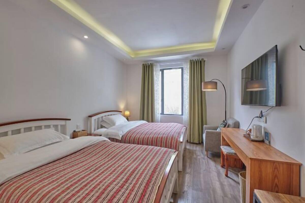 Une chambre d’hôtel avec deux lits, un bureau, une chaise, une télévision et une fenêtre avec des rideaux.