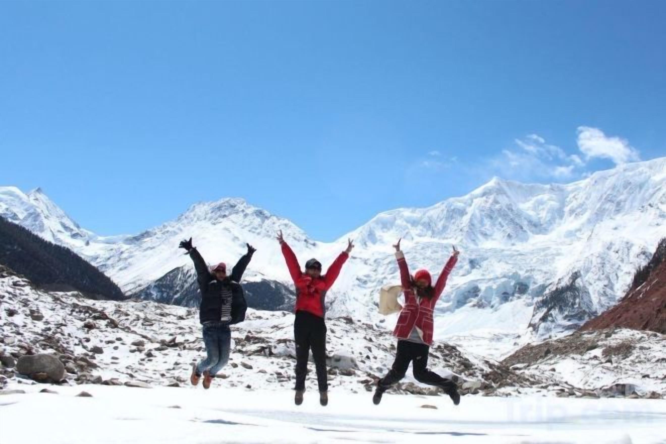 Three individuals jumping in a snowy mountainous area with clear skies.