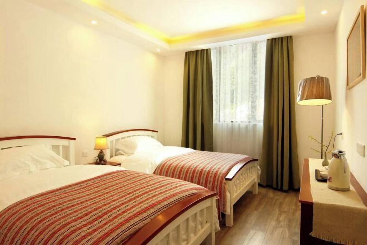 Une chambre d’hôtel avec deux lits, une table de chevet avec une lampe, une fenêtre avec des rideaux et un tableau accroché au mur.