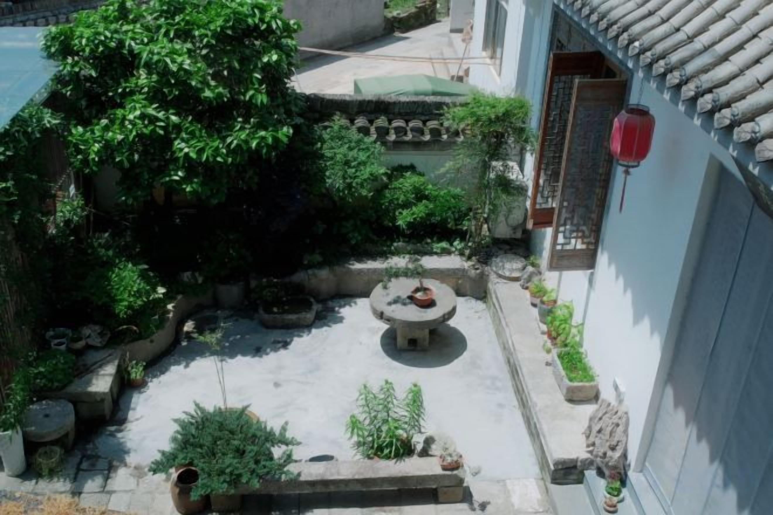 Un patio con un banco de piedra, plantas en macetas y un techo de tejas tradicionales.