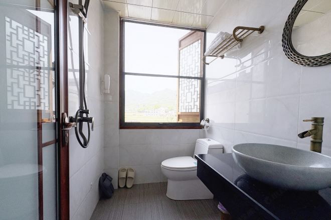 A bathroom with a toilet, a large sink, a window, and a shower area.