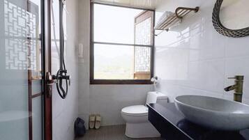 A bathroom with a toilet, a large sink, a window, and a shower area.