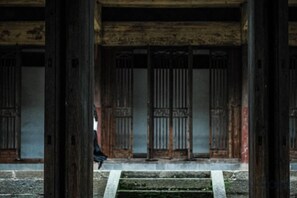 Un bâtiment traditionnel avec des colonnes en bois, et une personne qui marche au premier plan.