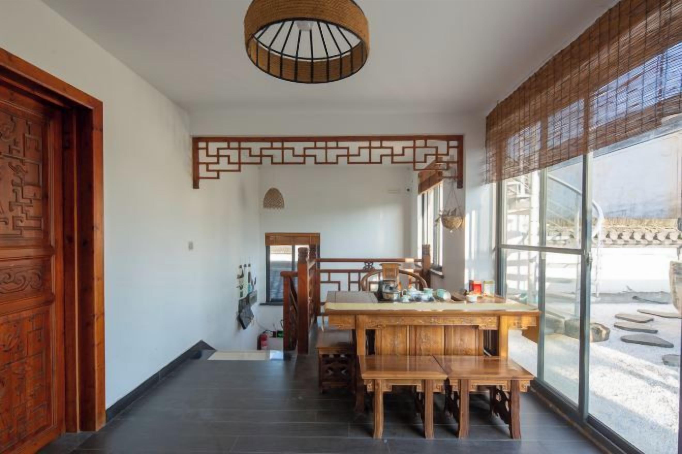 A traditional interior with a wooden dining table, a hanging light fixture, and a view through large windows.
