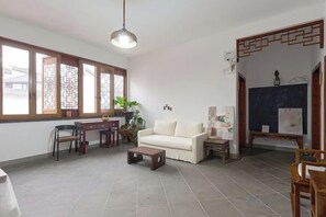 A living room with a sofa, a desk, and a chair. There is a large window with wooden frames and a hanging light fixture. - Longxingtang (Huangshan City)