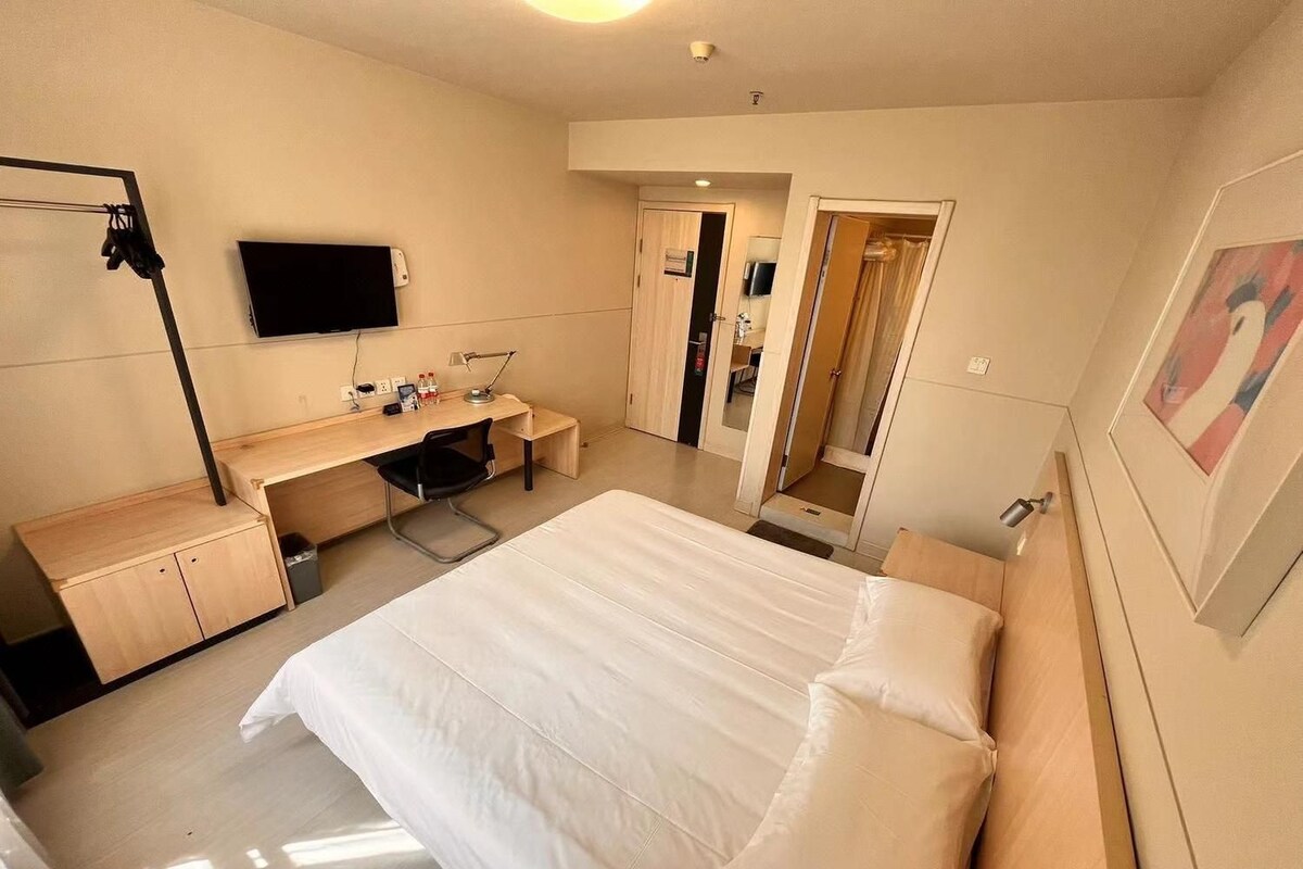 Ein Hotelzimmer mit einem Bett, einem Schreibtisch, einem Sessel, einem Fernseher und einer Tür zu einem Badezimmer.