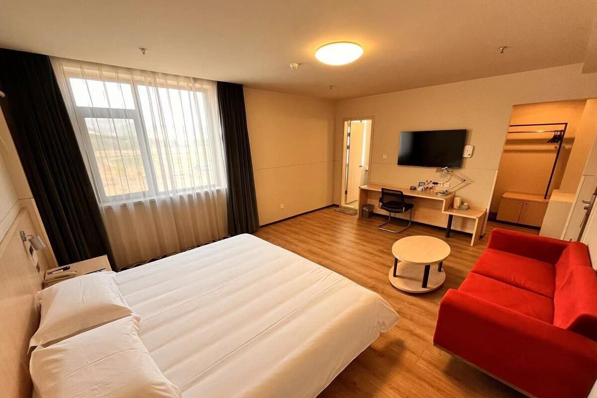 Ein Hotelzimmer mit Bett, Schreibtisch, Sessel, Fernseher und einem roten Sofa.
