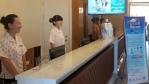 A reception desk with a digital screen displaying a photo, a counter, and a signboard with text. - Jinjiang Inn (Tianjin)