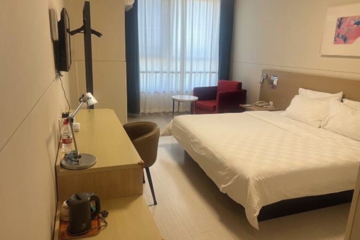 A hotel room with a bed, a desk, a chair, a small table, and a window with curtains.