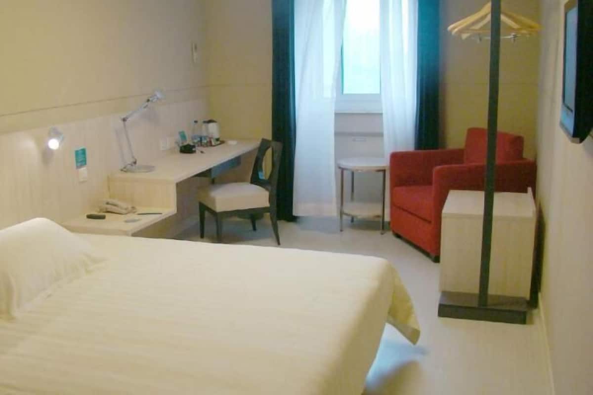 A hotel room with a bed, a desk, a chair, a small table, and a TV.