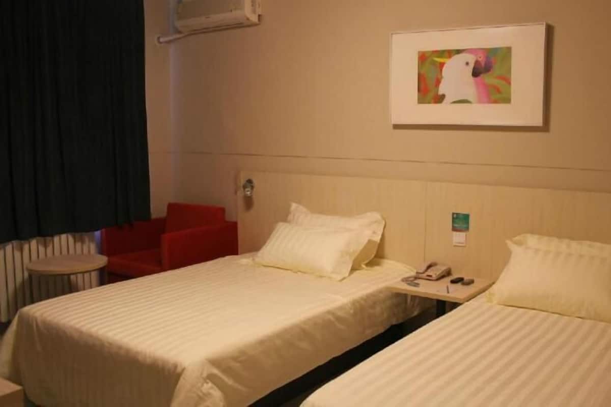 A hotel room with two beds, a red chair, a framed picture on the wall, and a small table with a phone and remote.