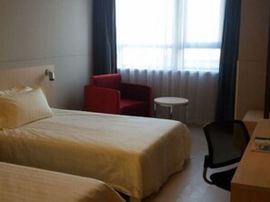 A hotel room with two beds, a red chair, a small round table, and a desk with a chair. - Jinjiang Inn (Tianjin)