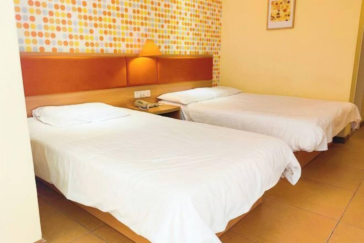 A hotel room with two single beds, a wooden headboard, a nightstand with a lamp, and a polka dot wall decoration.