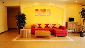 A living room with a red sofa, a wooden ottoman, and a coffee table. There are three framed pictures on the wall, a potted plant, and a television on a wooden cabinet. - Homeinn Pebble Hotel (Huludao Passenger Terminal) (Huludao)