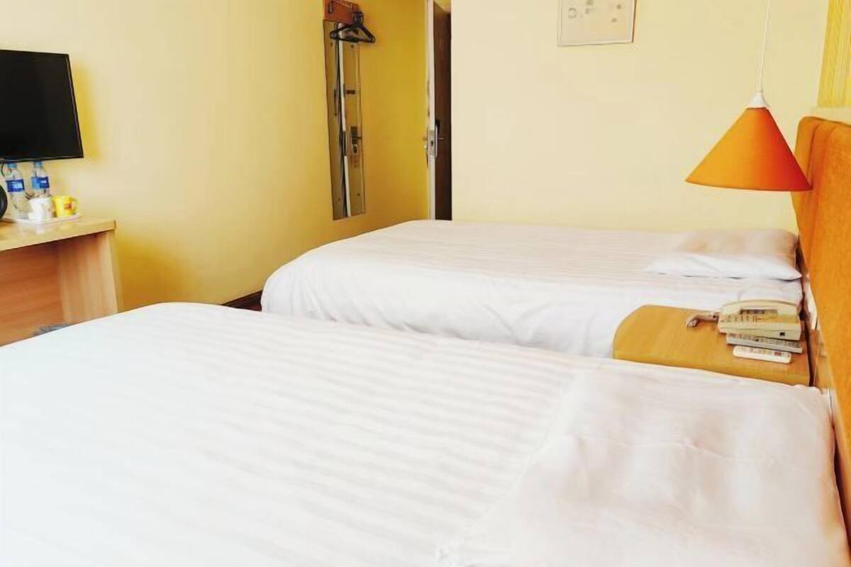 A hotel room with two beds, a TV, a shower, and a bedside table with a phone and books.