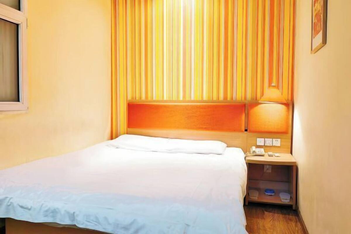 A hotel room with a bed, a nightstand, a lamp, and a window.