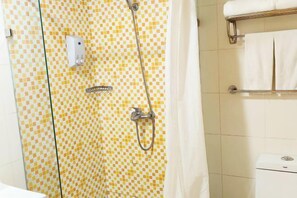 Une salle de bain avec un mur recouvert de carreaux à motifs, une douche équipée d’un pommeau de douche à main, un porte-serviettes avec des serviettes blanches et des toilettes dont on peut voir la marque.