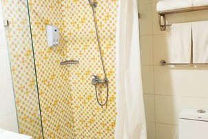 Un baño con pared de azulejos a cuadros, ducha con cabezal de ducha de mano, toallero con toallas blancas y un inodoro con etiqueta de marca visible.