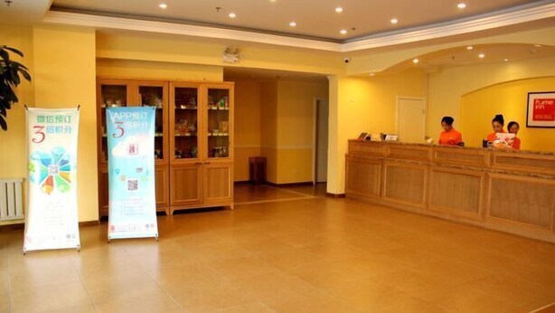 A hotel reception area with a wooden reception desk, a glass display cabinet, and a reception counter. There are two receptionists behind the counter. - Homeinn Pebble Hotel (Huludao Passenger Terminal) (Huludao)