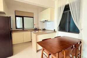 Een kleine keuken met een eethoek, een koelkast, een wastafel en een raam met gordijnen.