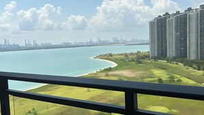 A high-rise building with a view of a coastal area, including a bridge and industrial structures in the distance.