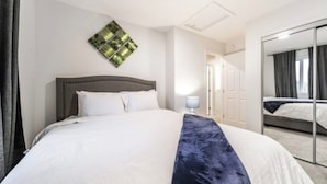 A hotel room with a large bed, a bedside table with a lamp, a mirror, and a wall-mounted artwork. - Soothing 3BDRM-King house near ice rink and golf course with WiFi in Stony Plain (Stony Plain)