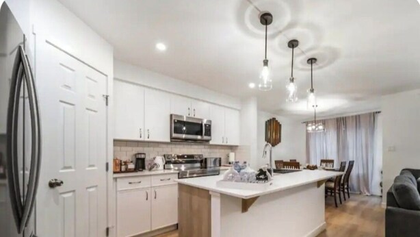 A modern kitchen with white cabinets, a central island, and a dining area with a gray sofa. - Soothing 3BDRM-King house near ice rink and golf course with WiFi in Stony Plain (Stony Plain)