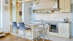 A modern kitchen with a central island, two bar stools, a built-in oven, and a coffee machine. - Čertovka by Interhome (Harrachov)