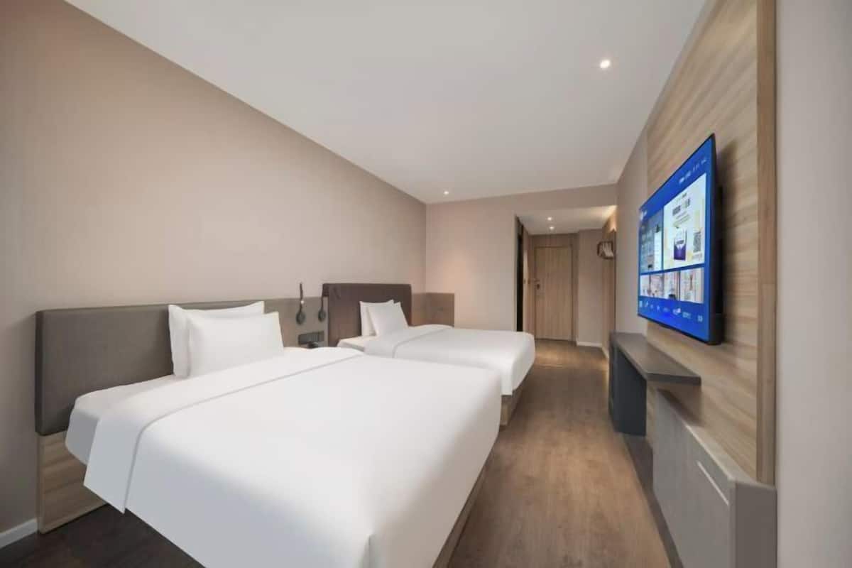 Habitación de hotel con dos camas, un televisor montado en la pared y piso de madera.