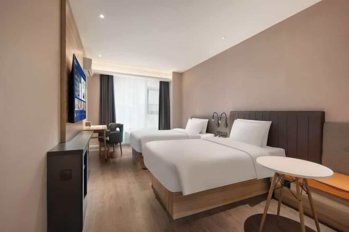 Una habitación de hotel con dos camas, un escritorio, una silla, un televisor y una mesita.