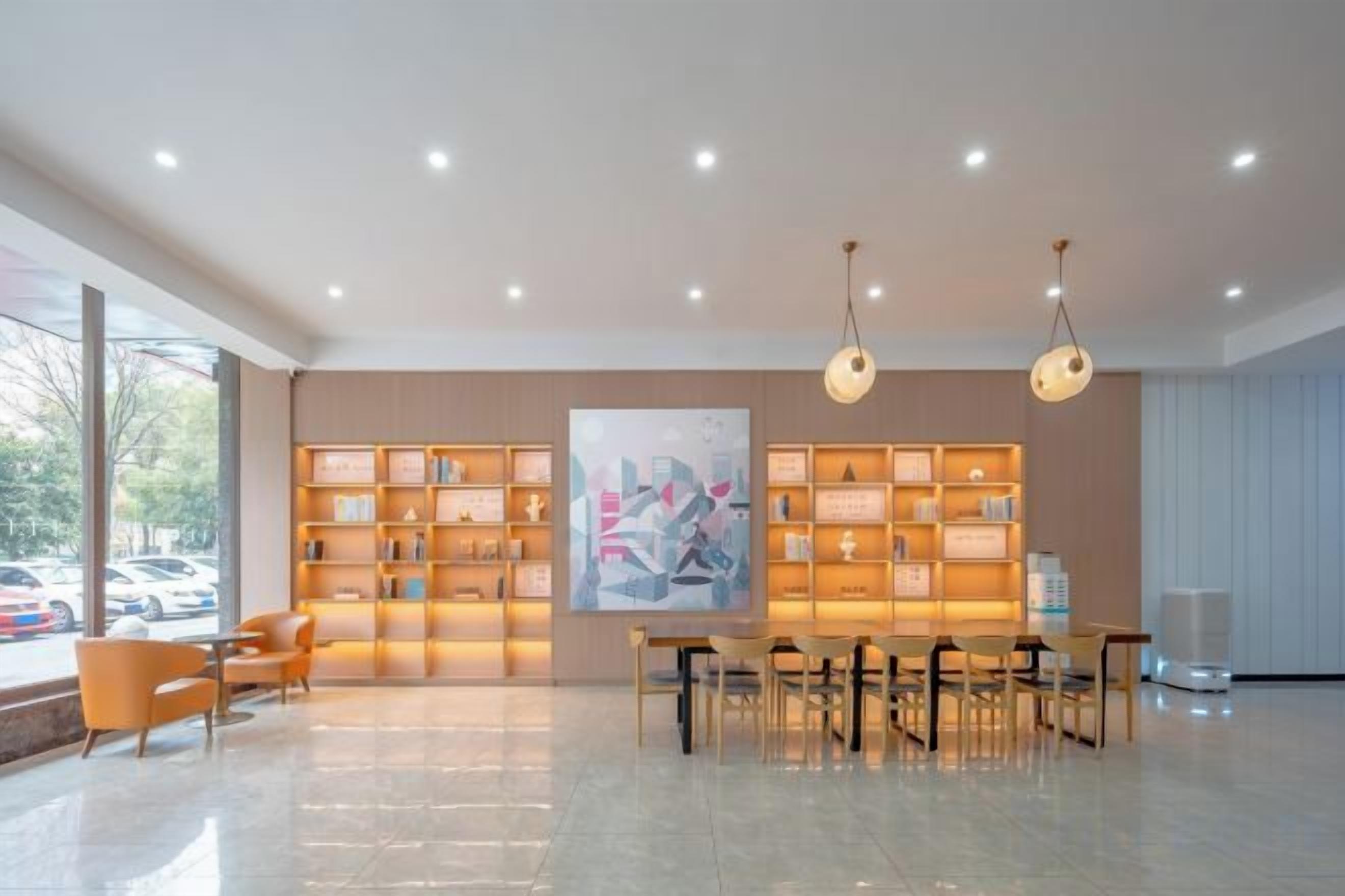 A spacious lobby with a high ceiling, a central dining area, and a large bookshelf filled with books.