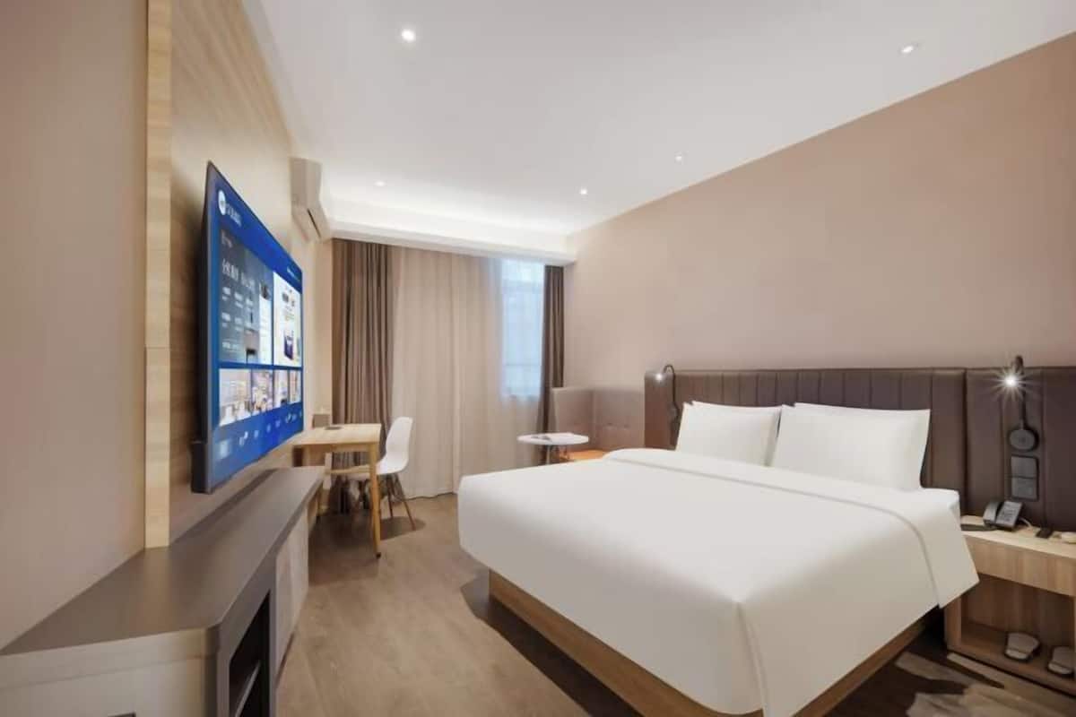Habitación de hotel con cama, escritorio, silla, televisión y una mesita.