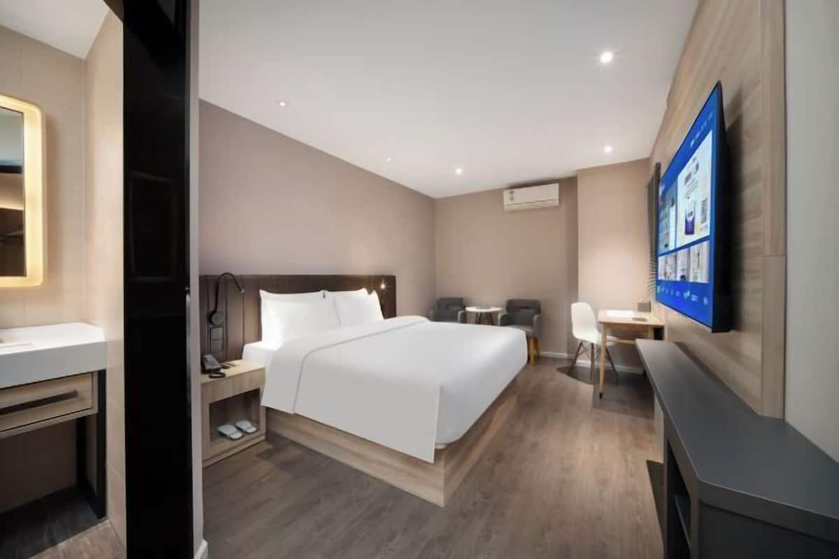 Un dormitorio moderno de hotel con cama, mesita de noche, silla, escritorio y televisor de pantalla plana montado en la pared.
